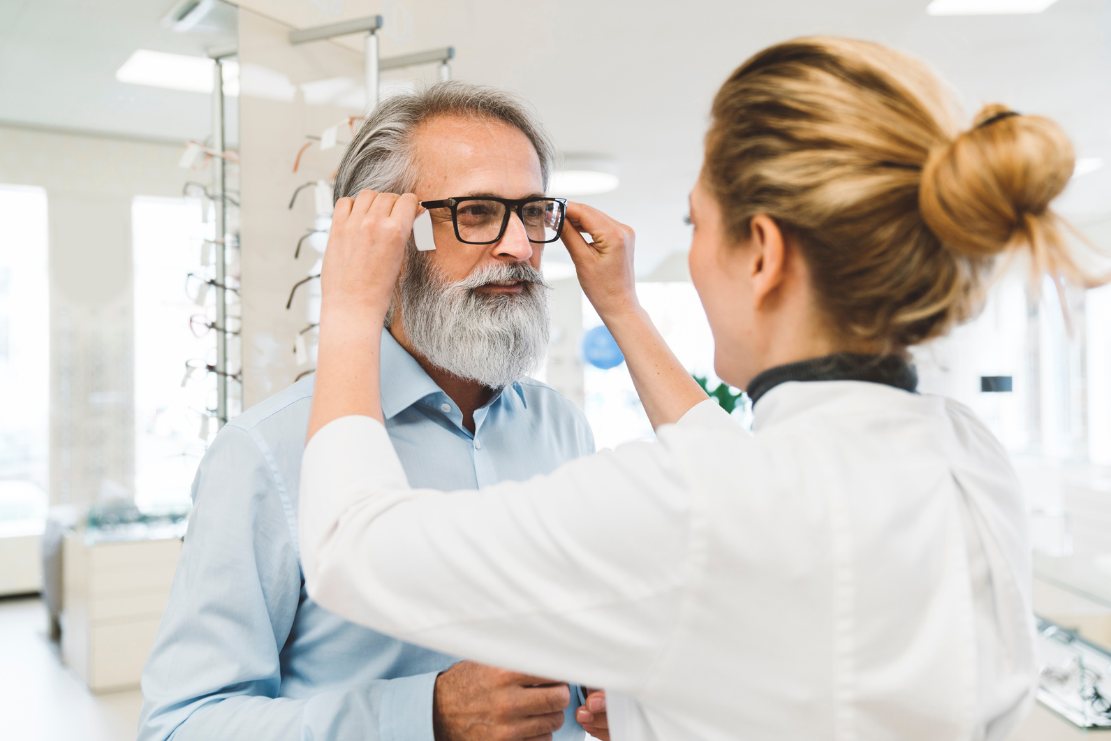 Saleswoman working in optics shop tying on prescription glasses on a costumer